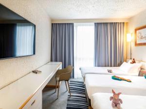 a hotel room with two beds and a tv at Hôtel Novotel Valenciennes in Valenciennes