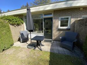 een patio met 2 stoelen, een tafel en een parasol bij Bungalows Hoefbos in Otterlo