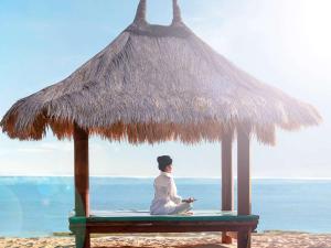 een persoon op een bankje onder een rieten parasol op het strand bij Novotel Lombok Resort & Villas in Kuta Lombok