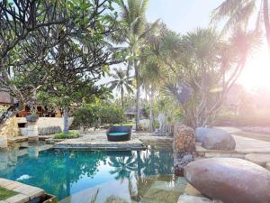 a swimming pool with palm trees in a backyard at Novotel Lombok Resort & Villas in Kuta Lombok