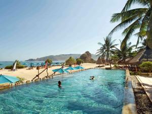 two people in a swimming pool next to a beach at Novotel Lombok Resort & Villas in Kuta Lombok