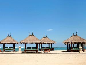 a group of picnic tables and straw umbrellas on a beach at Novotel Lombok Resort & Villas in Kuta Lombok