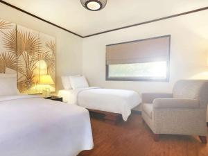 a hotel room with two beds and a chair at Novotel Lombok Resort & Villas in Kuta Lombok