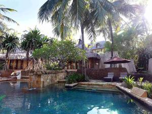 a swimming pool in front of a house with palm trees at Novotel Lombok Resort & Villas in Kuta Lombok