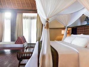 a bedroom with a canopy bed and a chair at Novotel Lombok Resort & Villas in Kuta Lombok