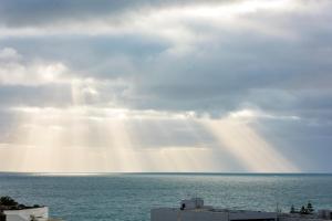 una vista del océano con el sol brillando a través de las nubes en Ramada by Wyndham VetroBlu Scarborough Beach en Perth