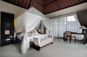 a bedroom with a canopy bed with a chair and a desk at Santi Mandala Villa & Spa in Sukawati