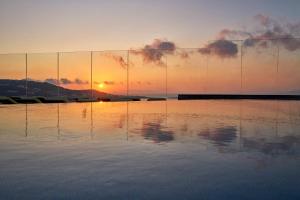 a sunset over a body of water with a lighthouse at Myconian Korali Relais & Chateaux in Mikonos