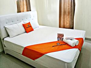 a white bed with an orange blanket and two pillows at WISMA ANDALI Syariah near RSUD Cideres in Majalengka