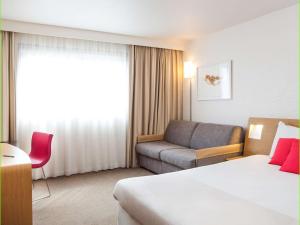 Novotel Paris La Defense Esplanade في كوربفوا: غرفه فندقيه بسرير واريكه