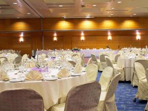 - une salle de banquet avec des tables, des chaises et du linge de maison blanc dans l'établissement Novotel Athens, à Athènes