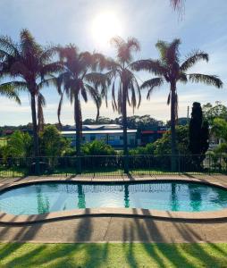 a pool with palm trees in front of a fence at Shellharbour Resort and Conference Centre in Shellharbour