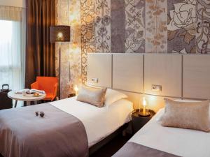 ブール・ガン・ブレスにあるMercure Bourg En Bresseのベッド2台とテーブルが備わるホテルルームです。