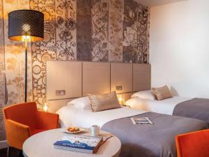 ブール・ガン・ブレスにあるMercure Bourg En Bresseのベッド2台、テーブルと椅子が備わるホテルルームです。