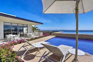a swimming pool with chairs and an umbrella next to a house at Luxe Cabo Condo w/ Ocean Views + Amenities! in Cabo San Lucas