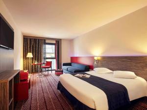 ブロワにあるホテル メルキュール ブロワ サントルの大きなベッドとソファが備わるホテルルームです。