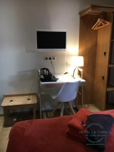 een slaapkamer met een bureau, een televisie en een bed bij Hotel la Turra in Termignon