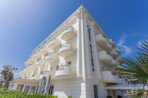 a white building with balconies and palm trees at Hotel Riviera in Milano Marittima