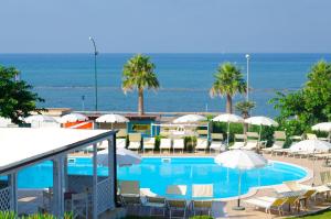 a swimming pool with chairs and umbrellas and the ocean at Eden Residence Club in Torre Ovo