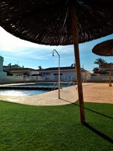 einen Strohschirm auf dem Rasen neben einem Pool in der Unterkunft Encantador adosado en Gran Alacant in Gran Alacant