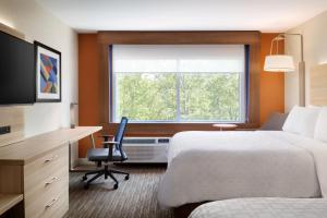 Holiday Inn Express & Suites - Grand Rapids South - Wyoming, an IHG Hotel في وايومنغ: غرفه فندقيه بسرير ومكتب ونافذه