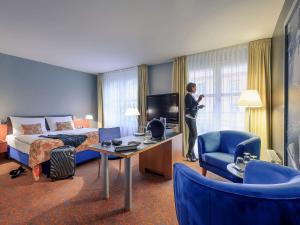 un uomo in piedi in una stanza d'albergo con un letto e una televisione di Mercure Hotel & Residenz Berlin Checkpoint Charlie a Berlino