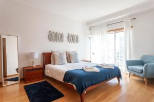 a white bedroom with a bed and a blue chair at Central Orient Residence - Modern, spacious and sunny! By the river! in Lisbon