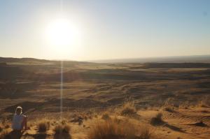a person sitting on a hill looking out at the desert at Namib Desert Campsite in Solitaire +2 photos