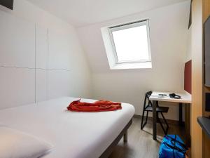 1 dormitorio con cama, escritorio y ventana en ibis budget Oostende Airport en Ostende