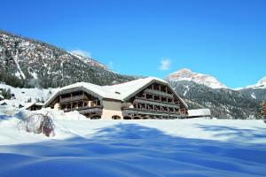 a building in the snow with mountains in the background at Hotel Rubino Deluxe in Campitello di Fassa