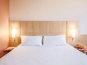 1 cama grande con sábanas blancas y 2 almohadas en Ibis Ripollet en Ripollet