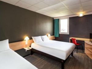 a hotel room with two beds and a desk and a table at ibis Lannion in Lannion