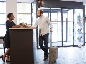 a man with a suitcase standing at a desk with a woman at Novotel Suites Cannes Centre in Cannes