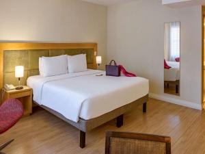 a bedroom with a large white bed and a red chair at Mercure Sao Paulo Jardins in São Paulo