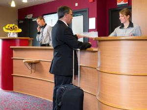 a man standing in front of a counter with two suitcases at ibis Brussels Waterloo in Waterloo