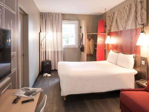 um quarto de hotel com uma grande cama branca e uma secretária em Ibis Madrid Fuenlabrada em Fuenlabrada