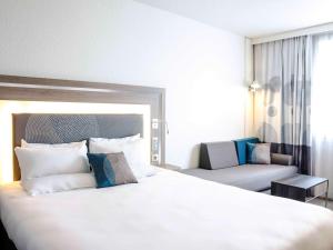 パリにあるノボテル パリ 17の白い大型ベッドとソファが備わるホテルルームです。