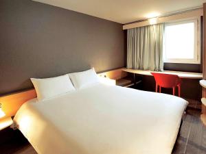 um quarto de hotel com uma cama branca e uma cadeira vermelha em Ibis Orly Chevilly Tram 7 em Chevilly-Larue