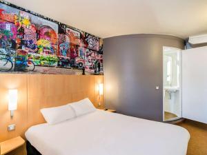 Un dormitorio con una cama blanca y una pintura en la pared en ibis Marne La Vallée Val d'Europe en Montévrain