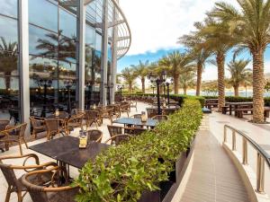 ein Restaurant mit Tischen, Stühlen und Palmen in der Unterkunft Ibis Abu Dhabi Gate in Abu Dhabi