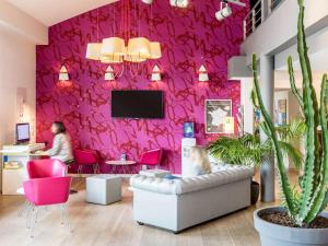 a room with a pink wall with a person sitting at a desk at ibis Styles Rennes St. Gregoire in Saint-Grégoire