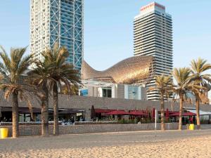 a building with palm trees in front of tall buildings at Ibis Barcelona Centro (Sagrada Familia) in Barcelona