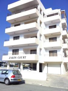 un edificio blanco con un coche aparcado delante de él en Zakos Court Apartments, en Lárnaca