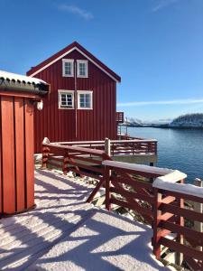 a red building with benches in front of a body of water at Henningsvær Rorbuer in Henningsvær +174 photos