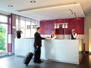 a man with a suitcase walking past a counter in an office at Mercure Hotel Düsseldorf City Nord in Düsseldorf