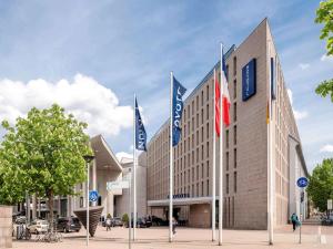 un grand bâtiment avec drapeaux devant lui dans l'établissement Novotel Freiburg am Konzerthaus, à Fribourg-en-Brisgau