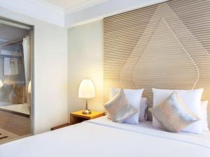 a bedroom with a bed with white pillows and a window at Novotel Semarang - GeNose Ready, CHSE Certified in Semarang