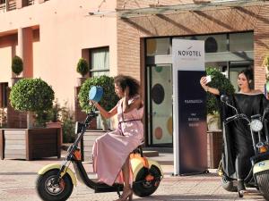 a woman in a dress is riding a scooter at Novotel Marrakech Hivernage in Marrakech