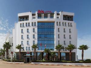 un grand hôtel blanc avec des palmiers devant lui dans l'établissement Ibis Casablanca Sidi Maarouf, à Casablanca