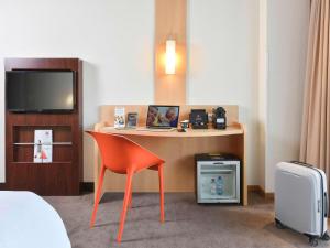 Habitación de hotel con escritorio con silla y TV. en ibis Kortrijk Centrum, en Cortrique